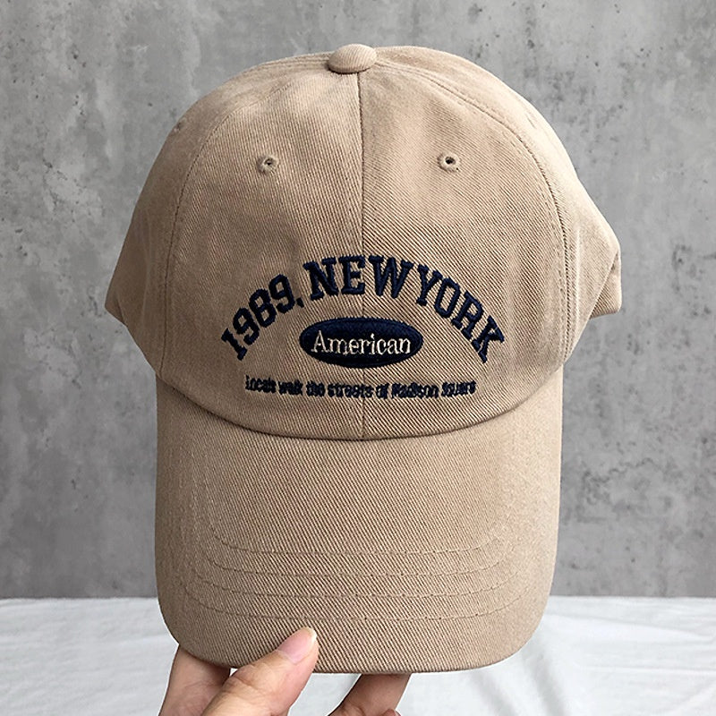 Beige cap with '1989 New York American' text on a gray background in Pakistan by Caps Nation