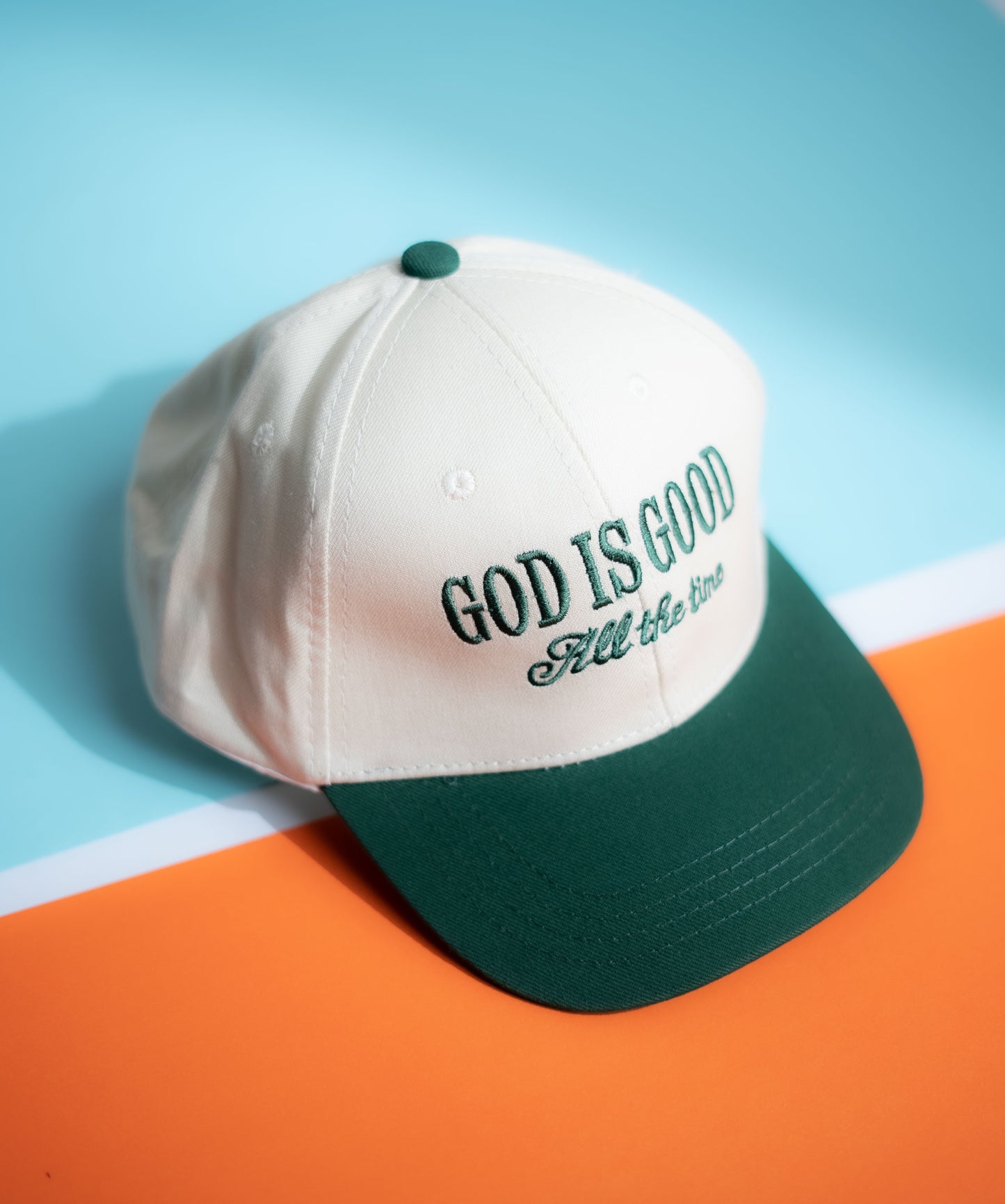 White and green cap with 'GOD IS GOOD All the time' text on a blue and orange background in Pakistan by Caps Nation