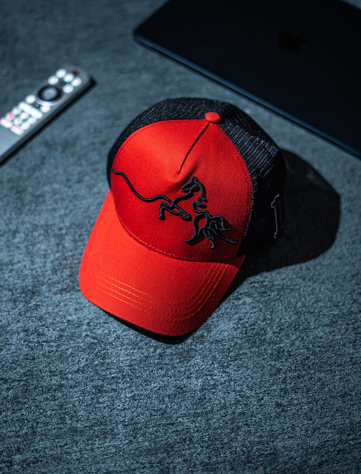 Red cap with black logo on a dark textured surface in Pakistan by Caps Nation.