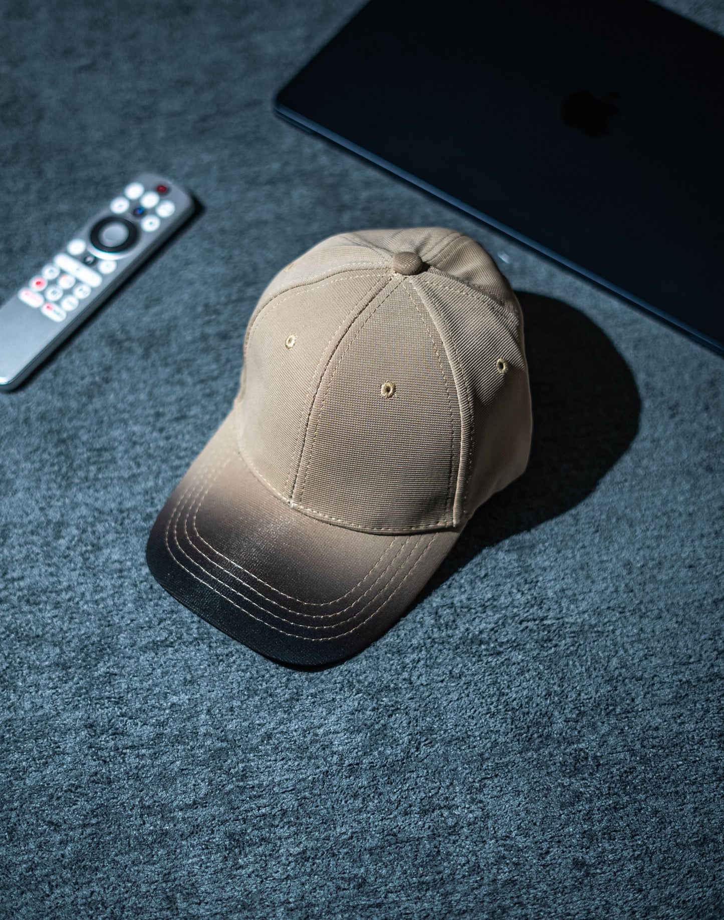 Brown cap on a dark textured surface with a remote control and electronic device in Pakistan by Caps Nation