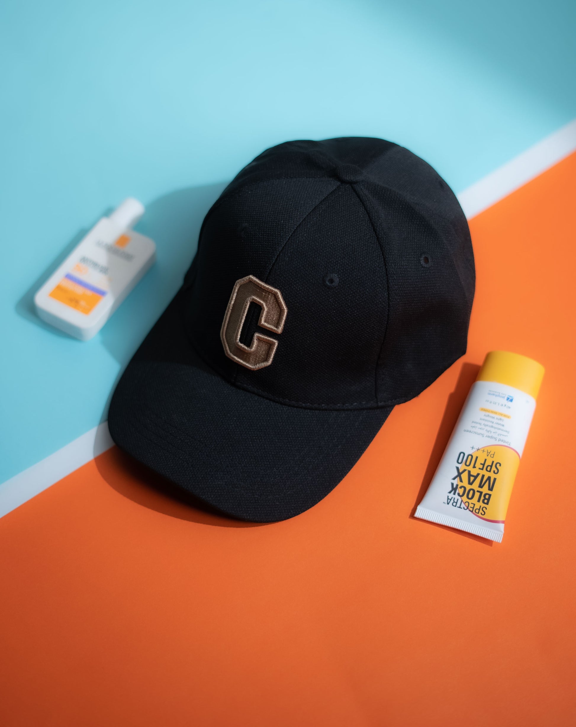 Black cap with a logo, sunscreen bottle, and stick on an orange and blue background in Pakistan by Caps Nation