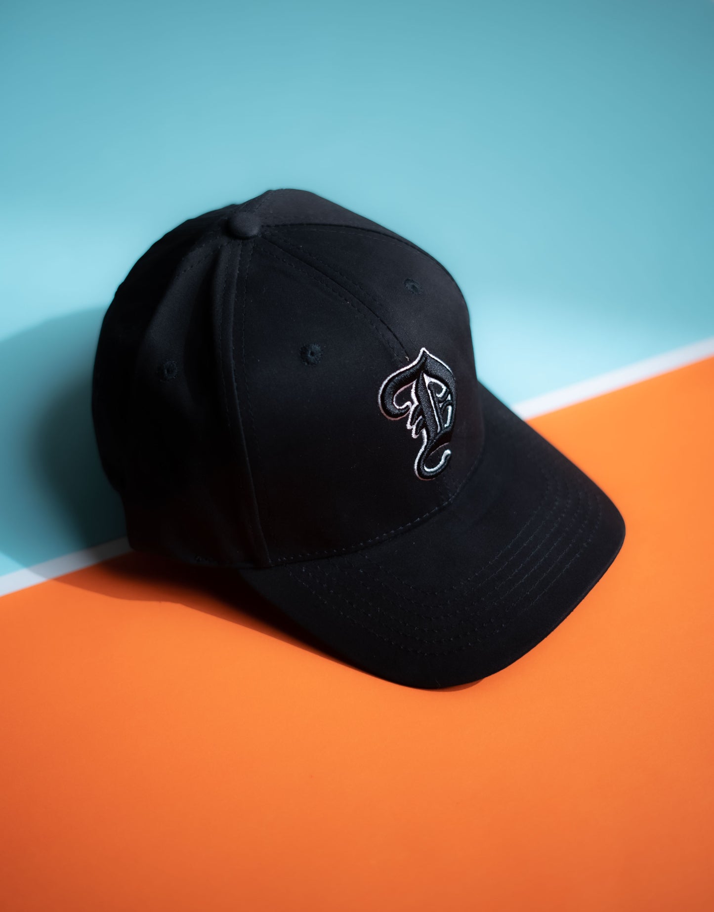 Black cap with a logo on an orange and blue background in Pakistan by Caps Nation