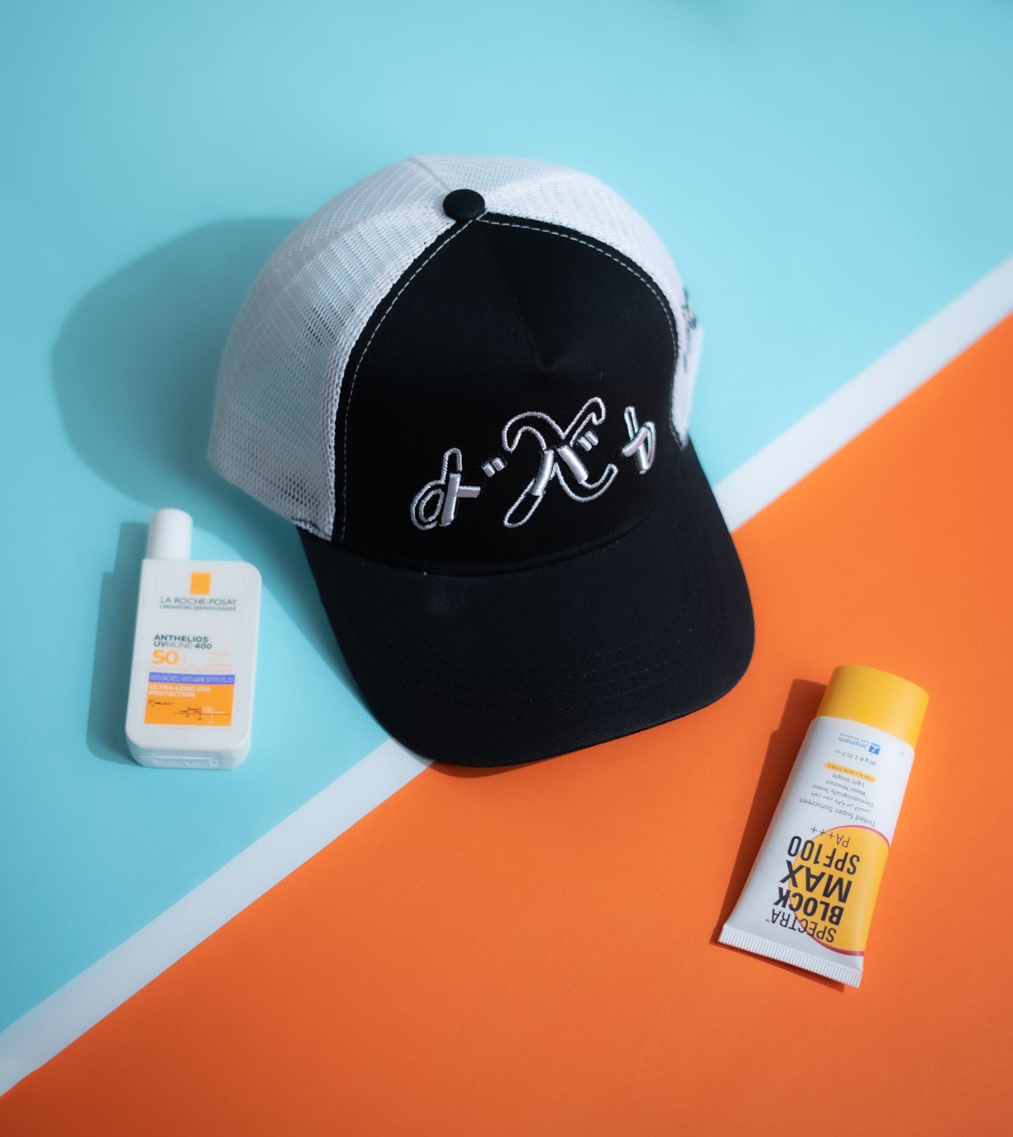 Black and white cap with Japanese text, bottle, and tube on a blue and orange background in Pakistan by Caps Nation