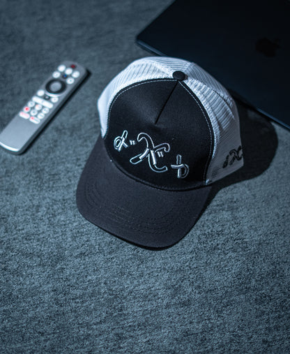 Black and gray cap with embroidered design on a dark surface with remote control and phone in Pakistan by Caps Nation
