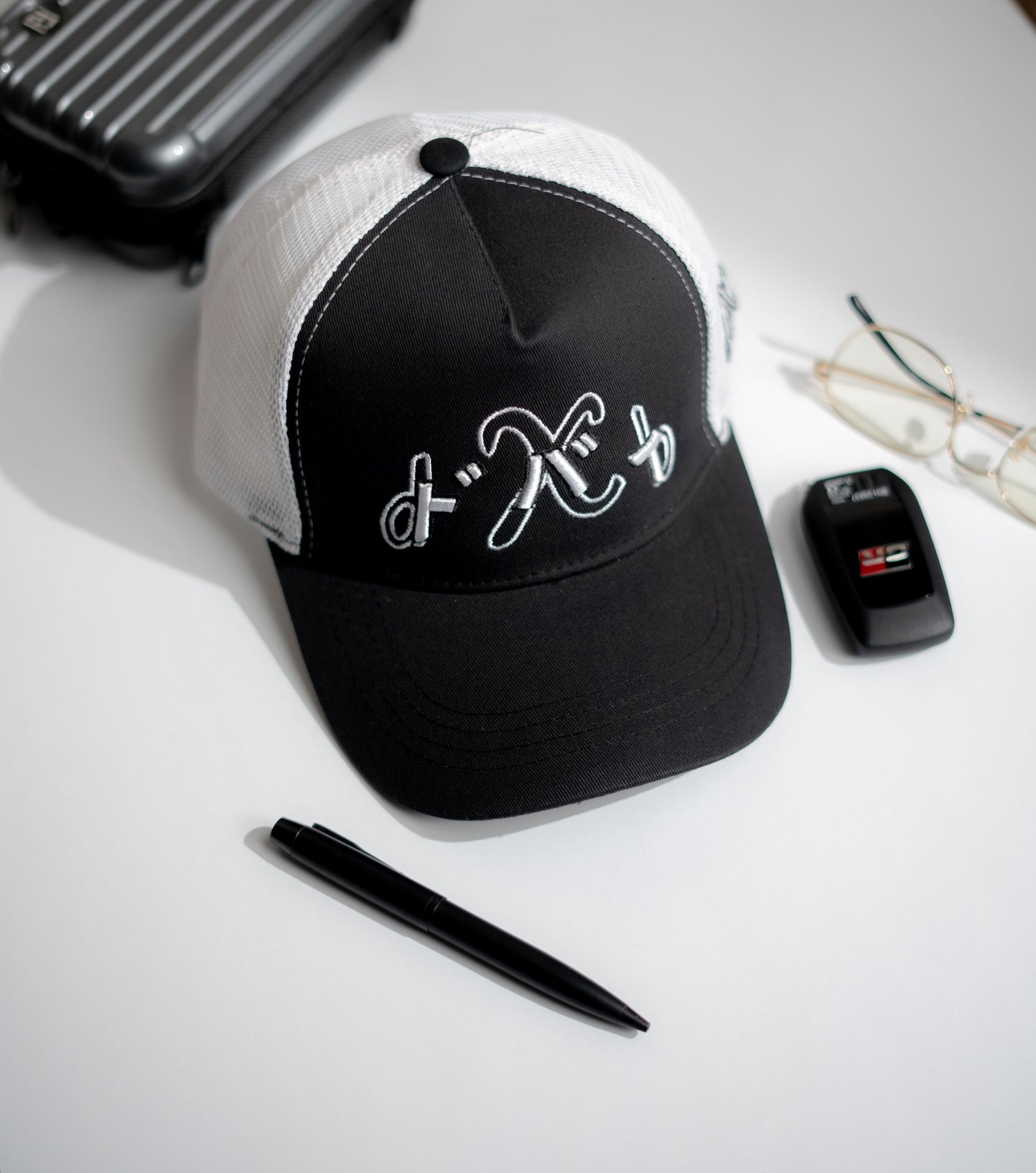 Black and white cap with a logo on a white surface with a pen and phone in Pakistan by Caps Nation
