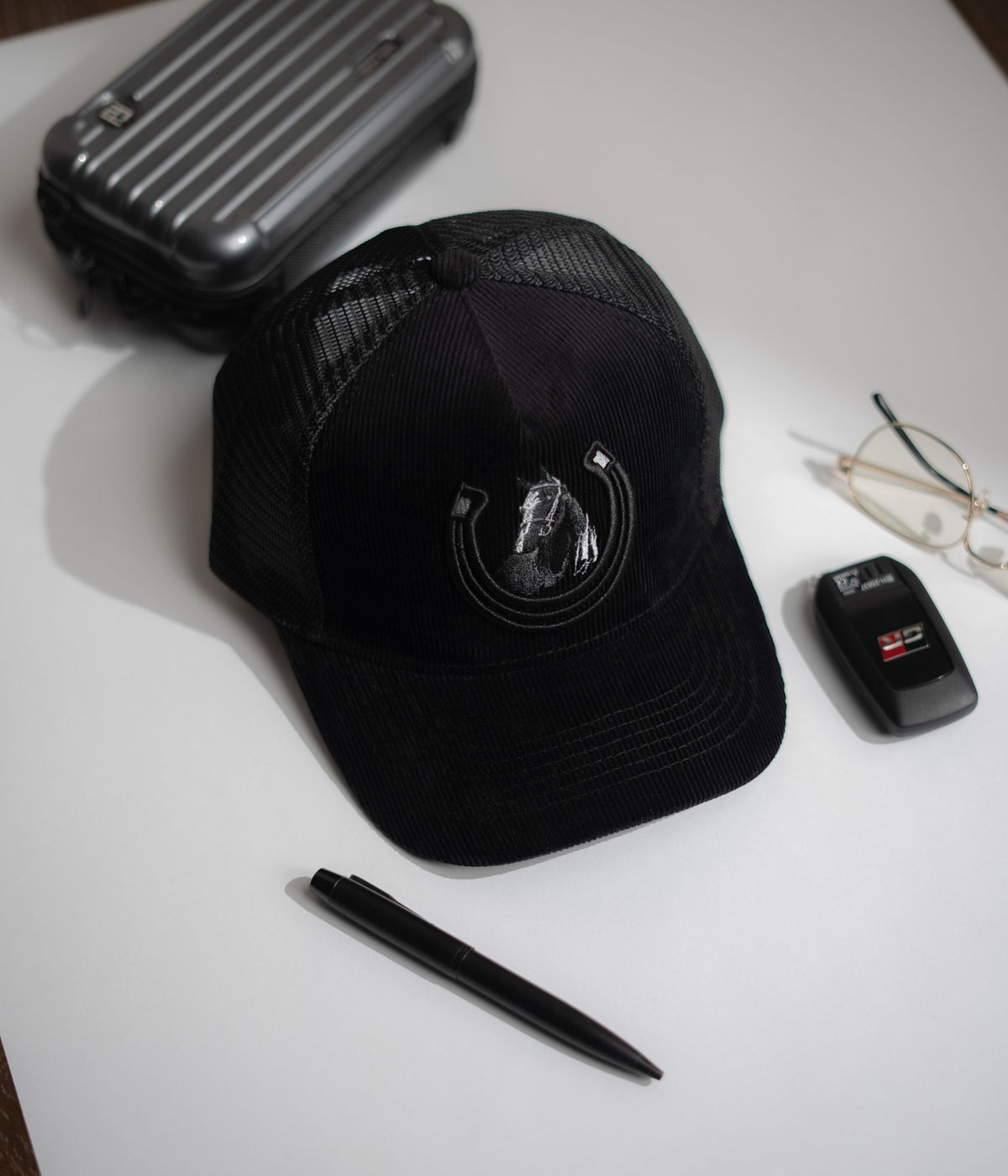 Black cap with a logo on a white surface with a pen, car key, and glasses in Pakistan by Caps Nation