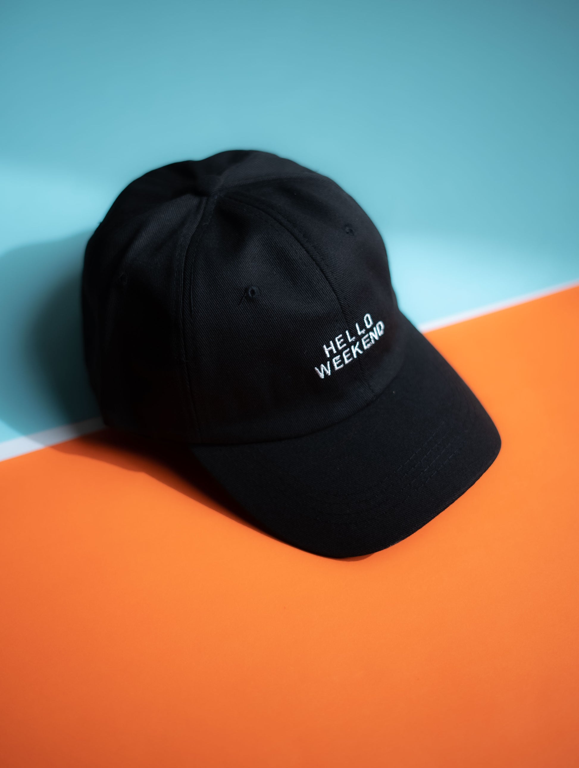 Black cap with 'HELLO WEEKEND' text on a blue and orange  background in Pakistan by Caps Nation