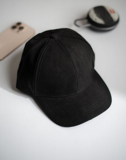 Black cap on a white surface with a phone and small round object in the background in Pakistan by Caps Nation