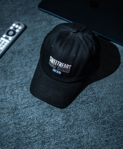 Black cap with text on a dark textured surface with remote control and laptop in Pakistan by Caps Nation