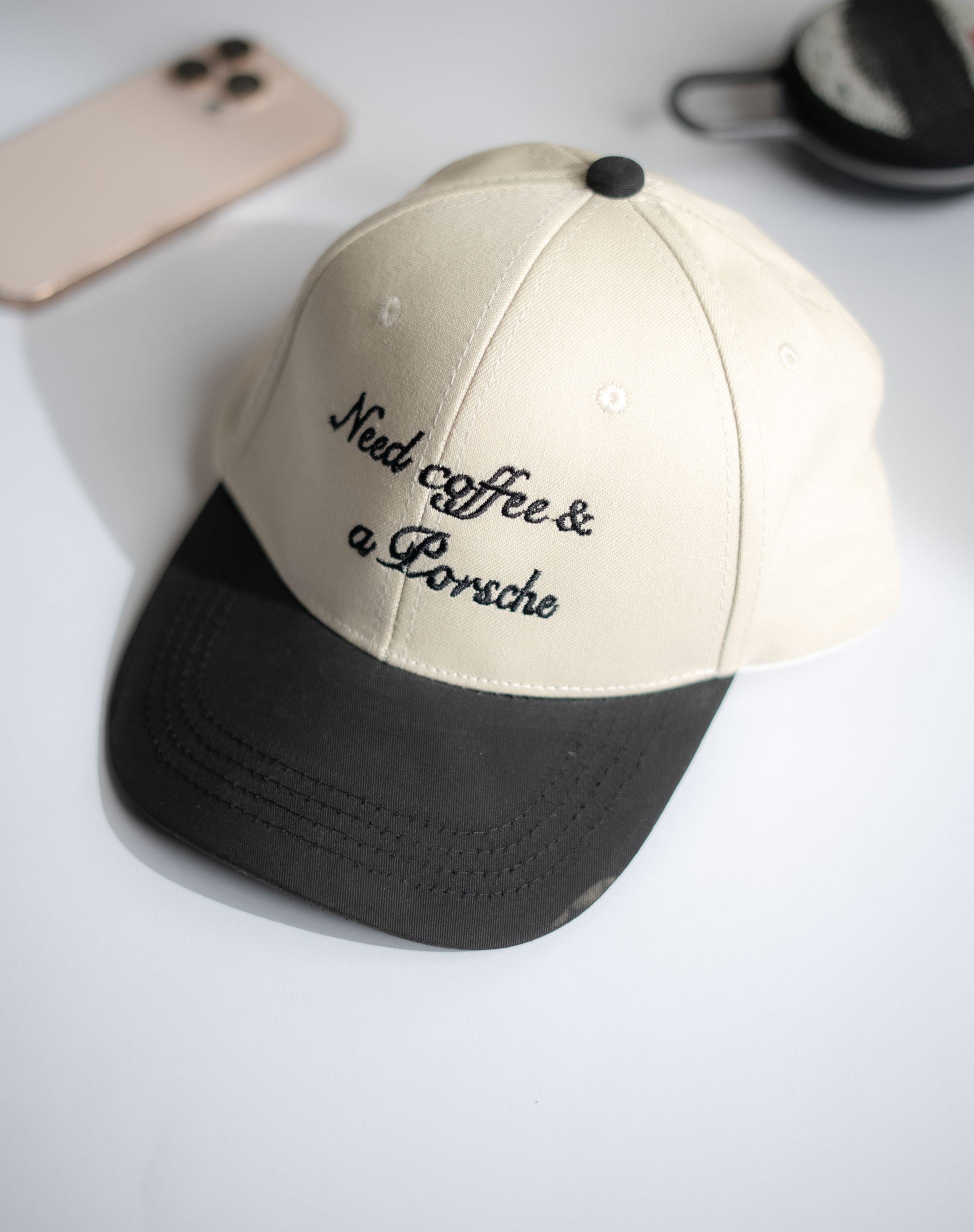 Beige and black cap with 'Need coffee & a Porsche' text on a light gray background in Pakistan by Caps Nation