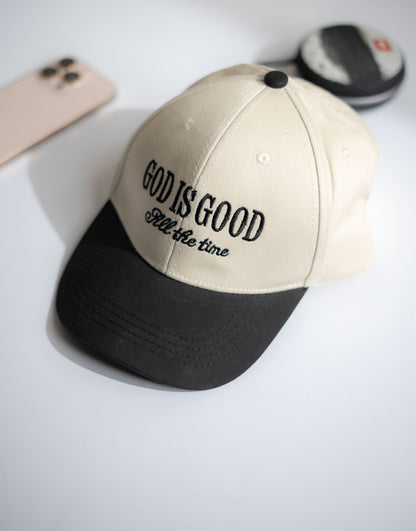 Beige and black cap with 'God is good all the time' text on a white surface in Pakistan by Caps Nation