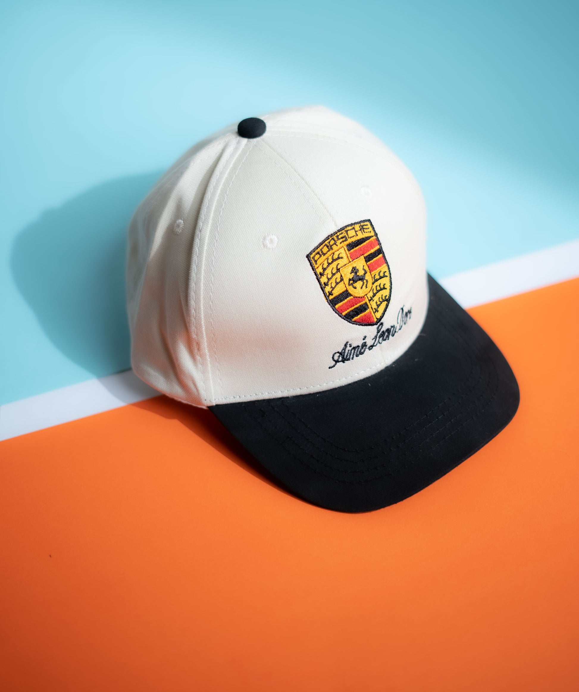 White and black cap with Porsche logo on a blue and orange background in Pakistan by Caps Nation