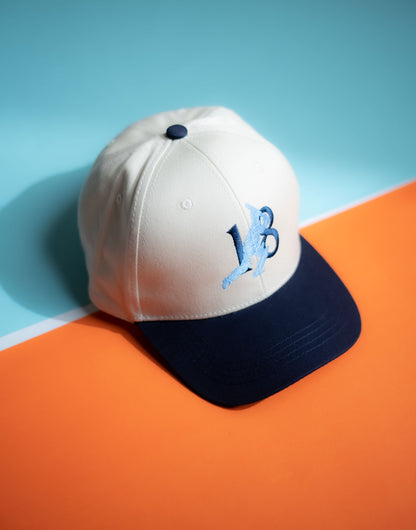 White and navy cap with a logo on an orange and blue background in Pakistan by Caps Nation