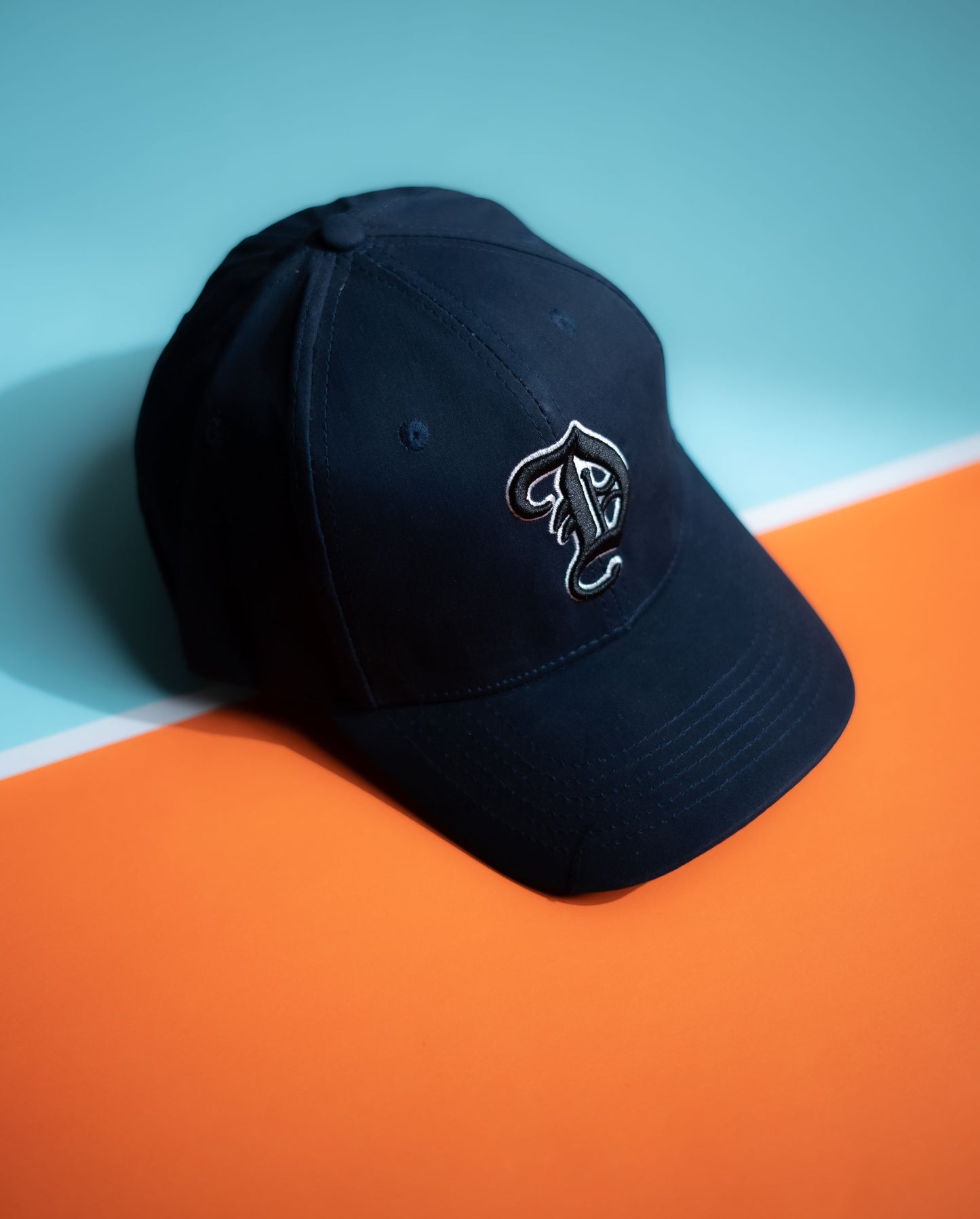 Black cap with a logo on an orange and blue background in Pakistan by Caps Nation