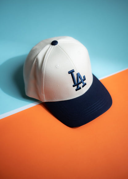 White baseball cap with navy bill and LA logo on a blue and orange background in Pakistan by Caps Nation