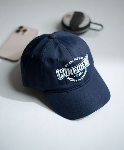 Navy blue cap with white text on a light gray surface with phone and case in the background in Pakistan by Caps Nation