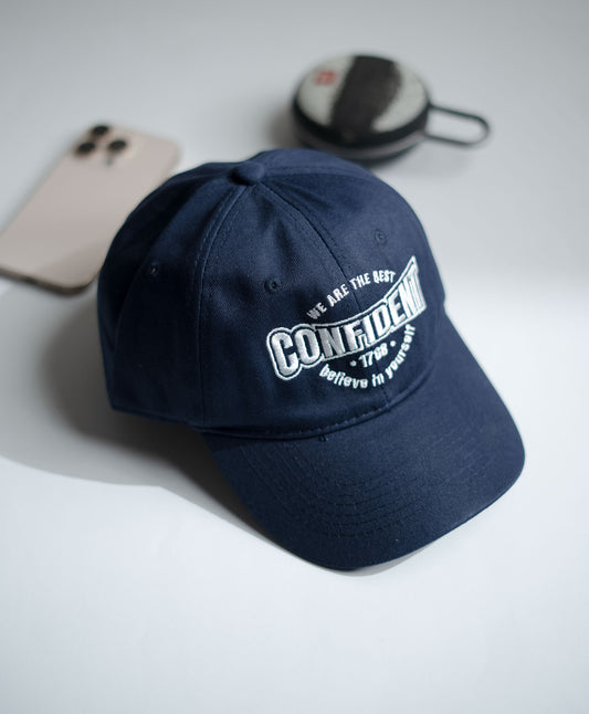Navy blue cap with white text on a light gray surface with phone and case in the background in Pakistan by Caps Nation