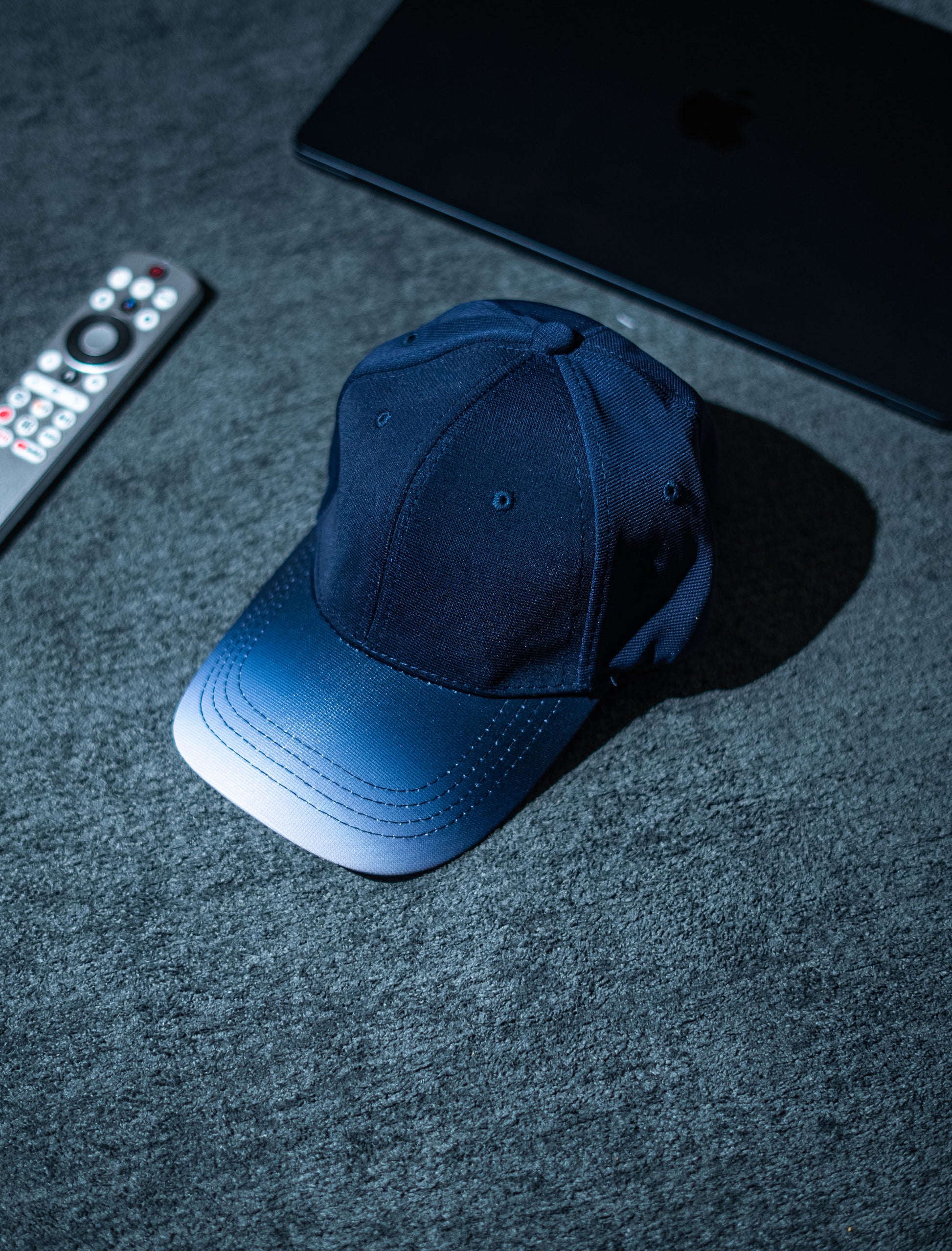 Blue cap on a dark textured surface with a remote control and electronic device in the background in Pakistan by Caps Nation