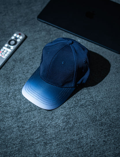 Blue cap on a dark textured surface with a remote control and electronic device in the background in Pakistan by Caps Nation