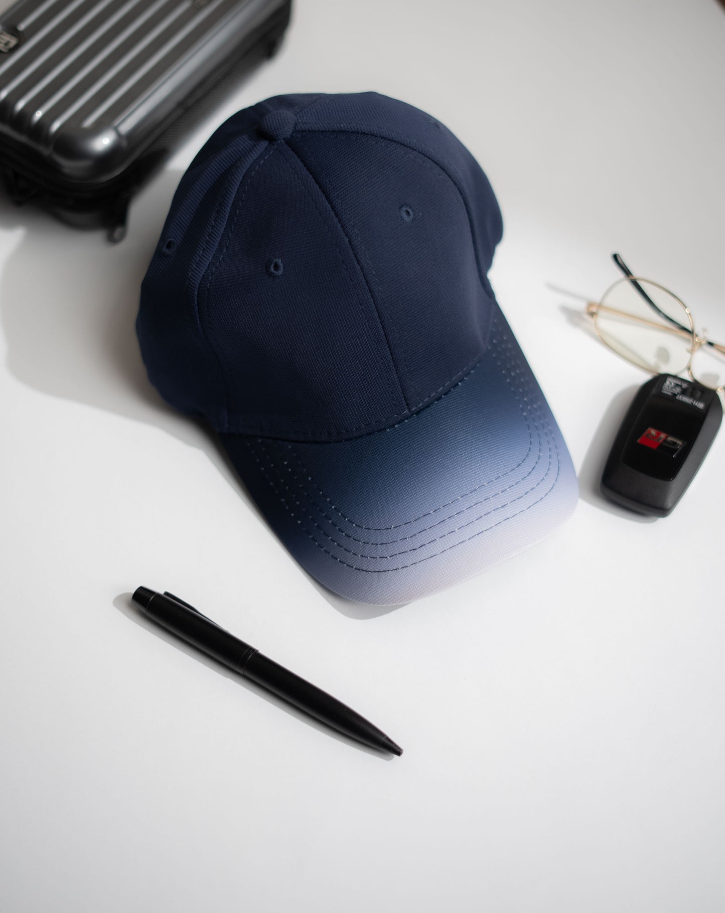 Navy blue cap, black pen, car key fob, and sunglasses on a white surface in Pakistan by Caps Nation