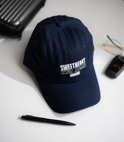 Navy blue cap with text on a white surface with a pen, glasses, and black case in Pakistan by Caps Nation