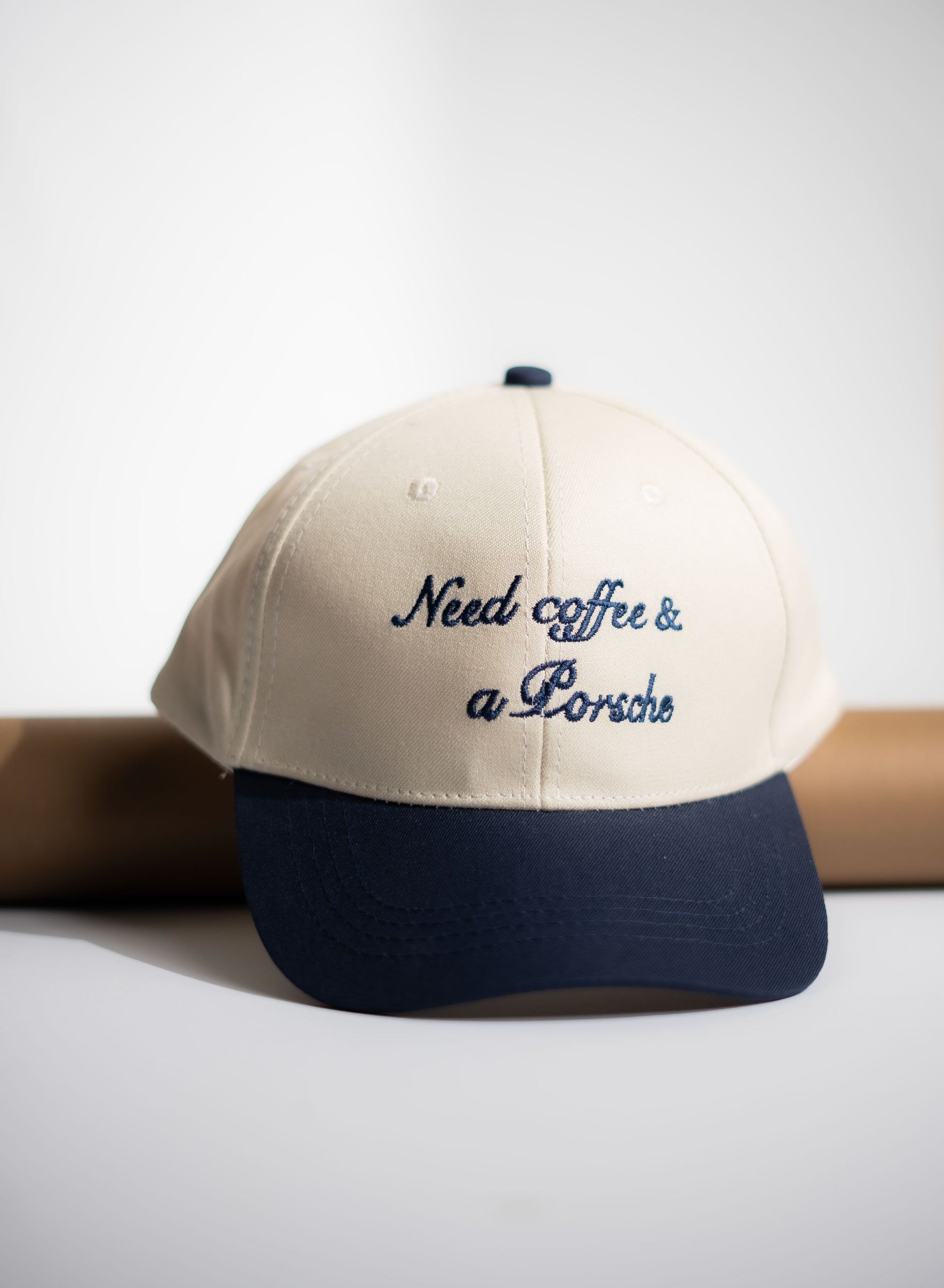 Beige and navy cap with 'Need coffee & a Porsche' text on a white background in Pakistan by Caps Nation
