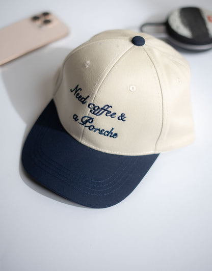 Beige and navy cap with 'Need coffee & a Porsche' text on a white surface in Pakistan by Caps Nation