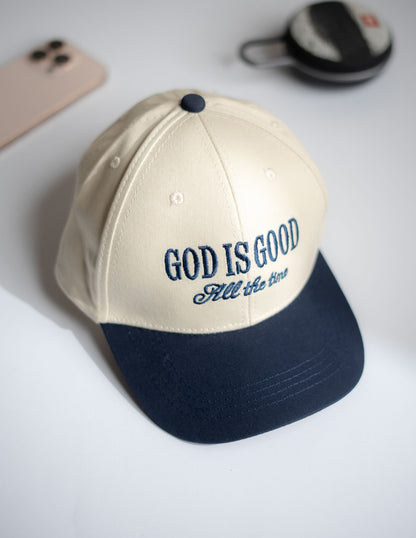 Beige and navy cap with 'God is Good All the Time' text on a white surface in Pakistan by Caps Nation