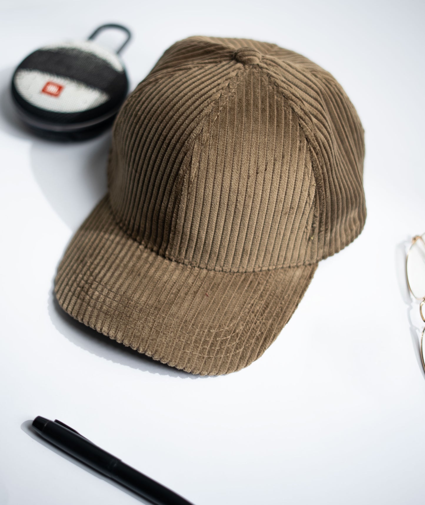 Beige corduroy cap on a white background with a pen and small round object in Pakistan by Caps Nation