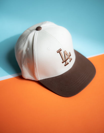 White and brown baseball cap with LA logo on a blue and orange background in Pakistan by Caps Nation
