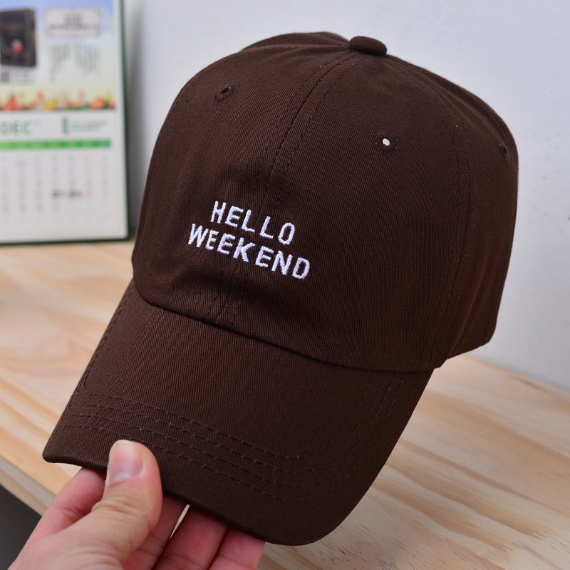 Brown cap with 'HELLO WEEKEND' text held by a hand on a wooden  surface in Pakistan by Caps Nation