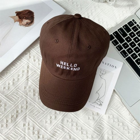 Brown cap with 'Hello Weekend' text on a desk with a laptop and magazine in Pakistan by Caps Nation