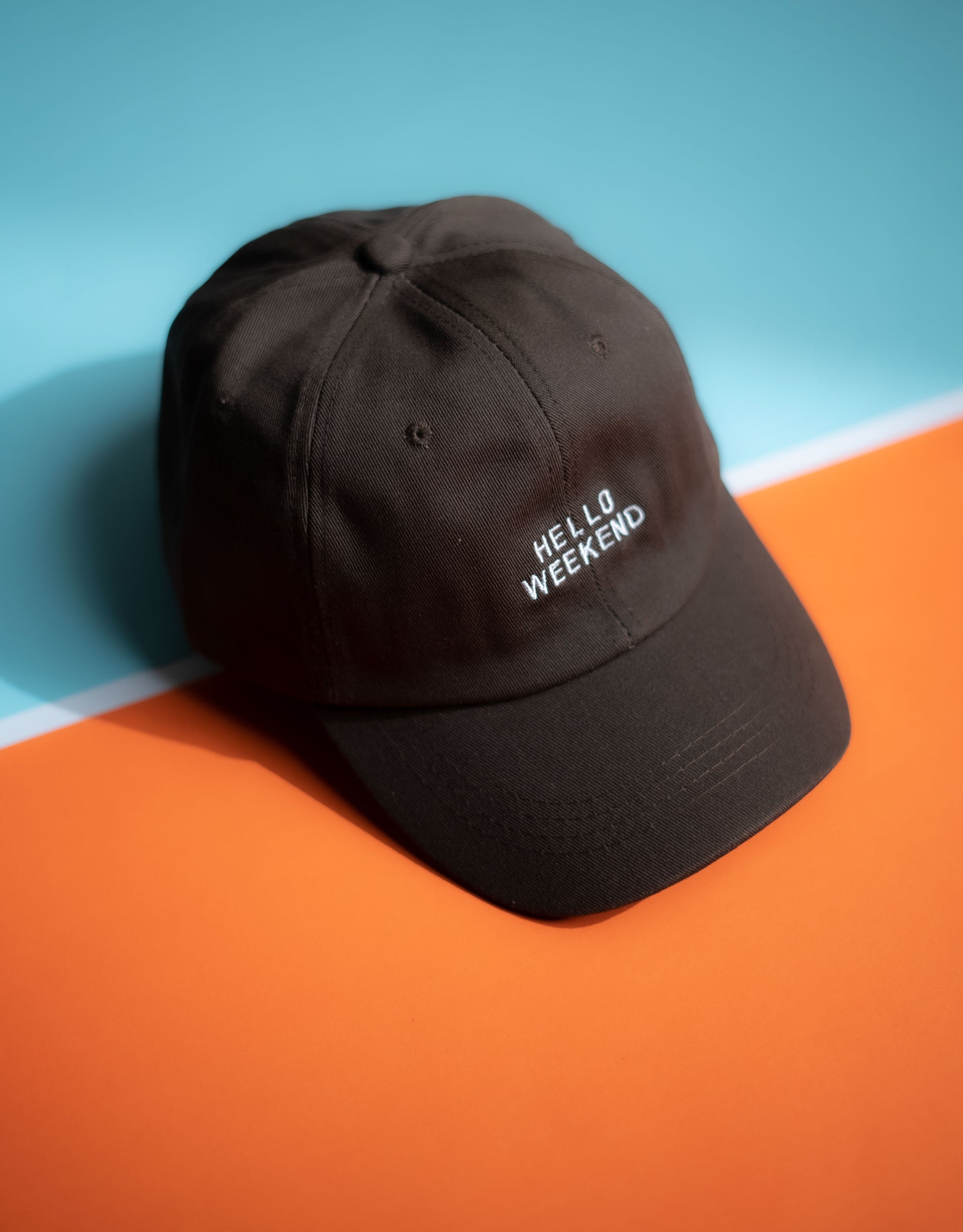 Black cap with 'Hello Weekend' text on a blue and orange background in Pakistan by Caps Nation