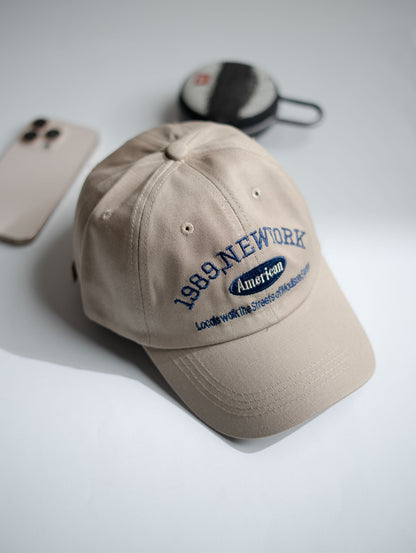 Beige cap with text on a light gray surface with phone and wallet in Pakistan by Caps Nation