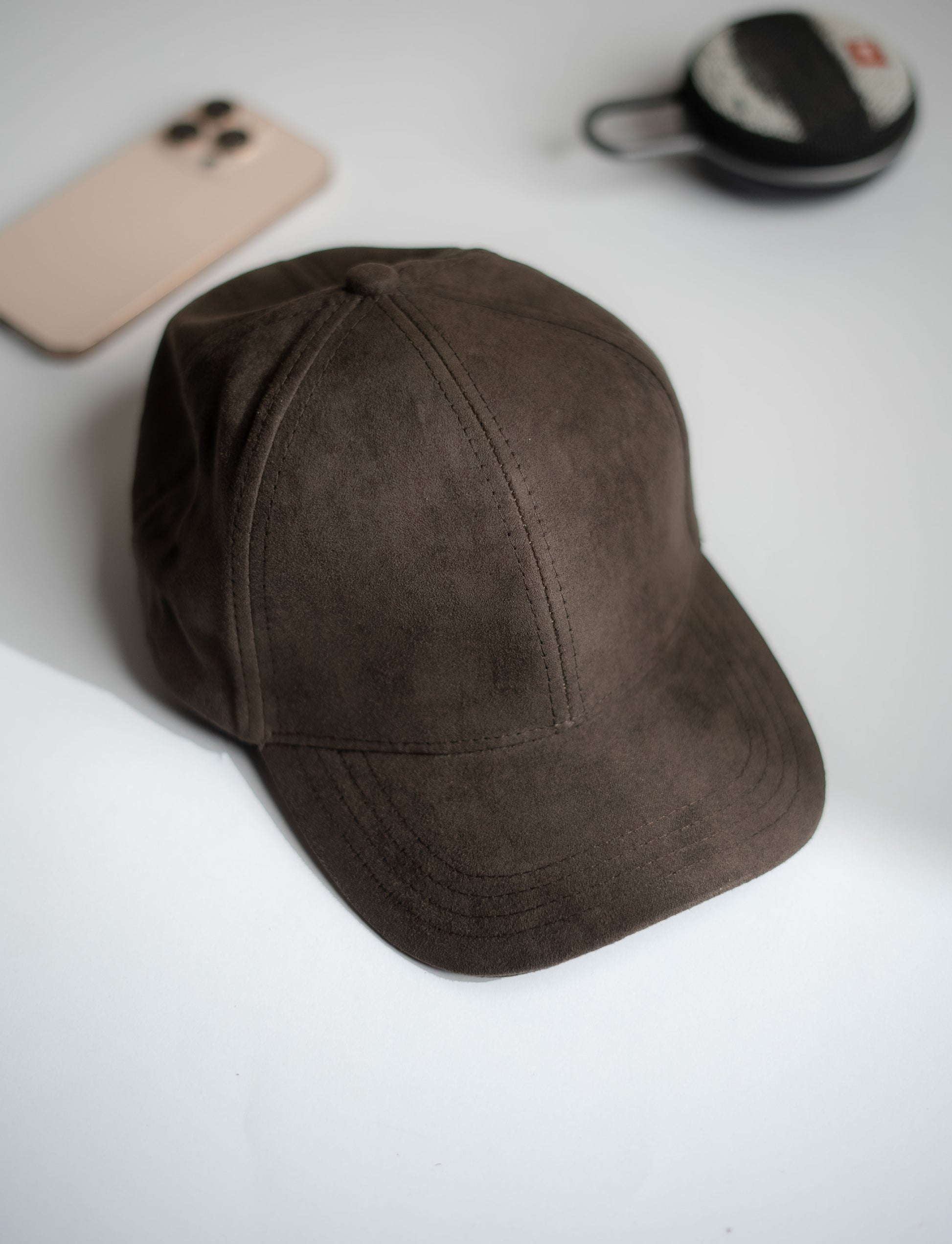 Brown cap on a white surface with a phone and mirror in the background in Pakistan by Caps Nation