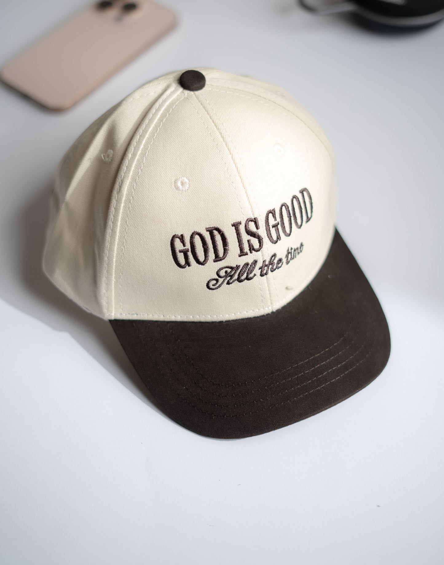 Beige and brown cap with 'God is Good All the Time' text on a white surface in Pakistan by Caps Nation