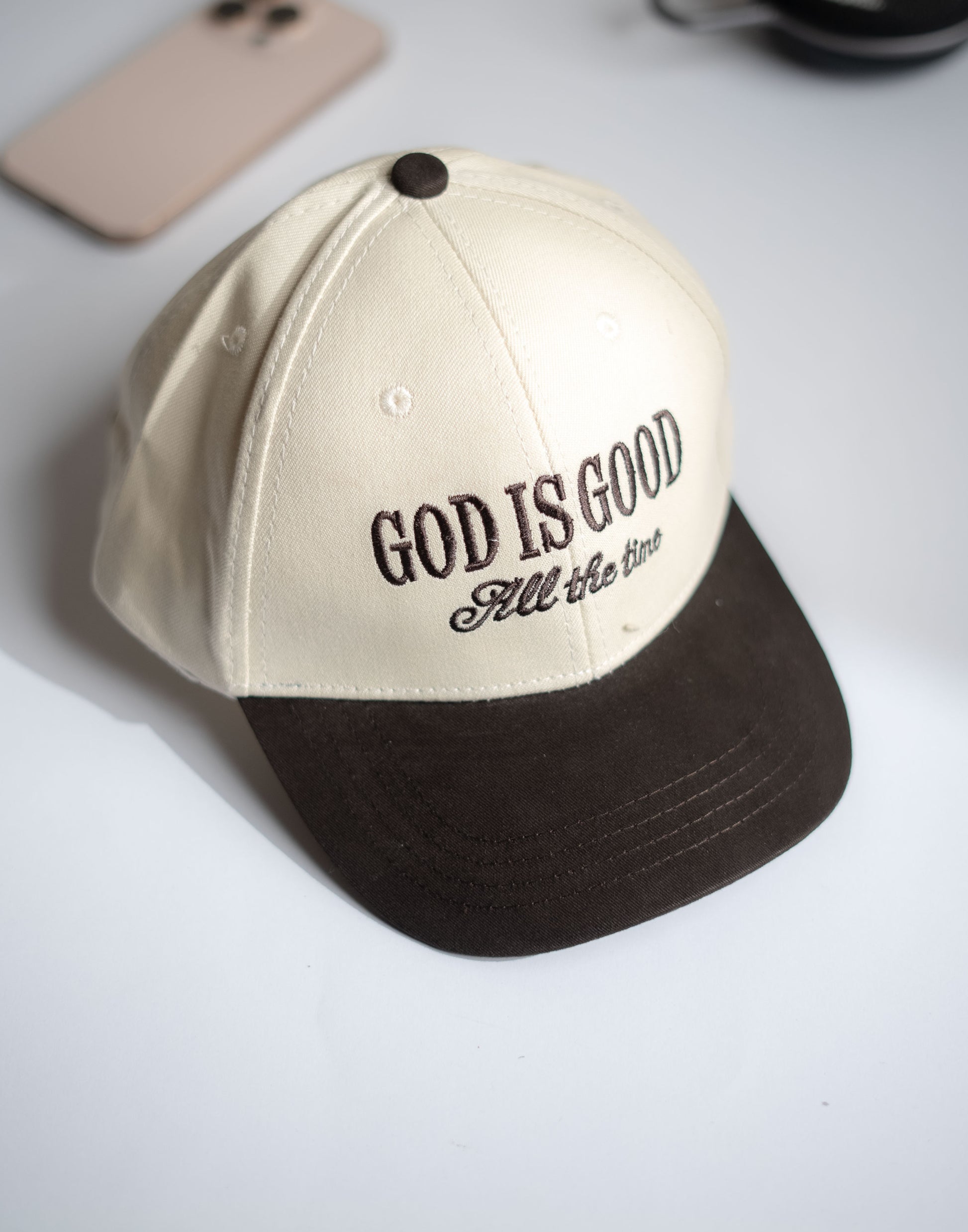 Beige and brown cap with 'God is Good All the Time' text on a white surface in Pakistan by Caps Nation