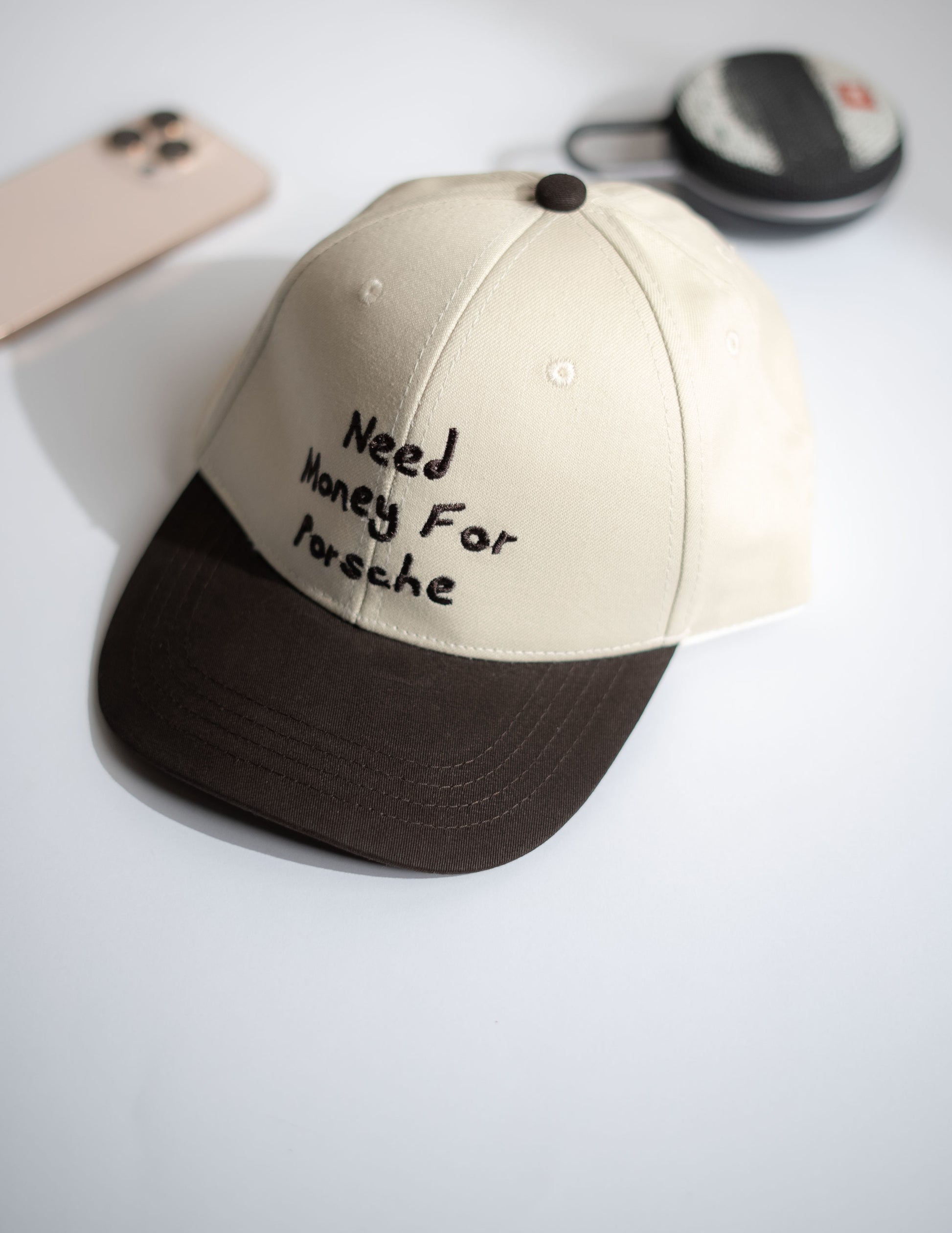 Beige and brown cap with 'Need Money For Porsche' text on a white surface in Pakistan by Caps Nation