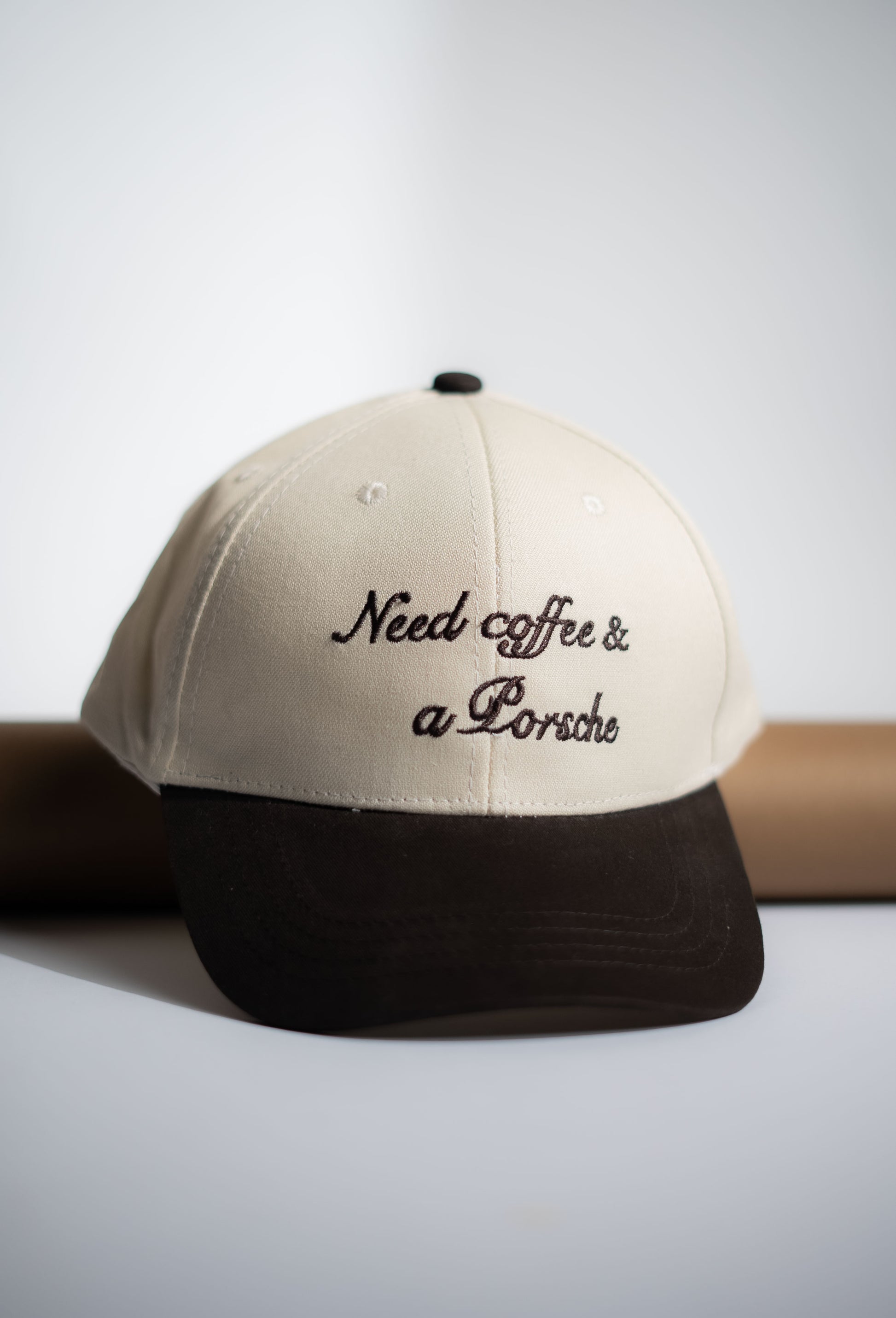 Beige and black cap with 'Need coffee & a Porsche' text on a light background in Pakistan by Caps Nation