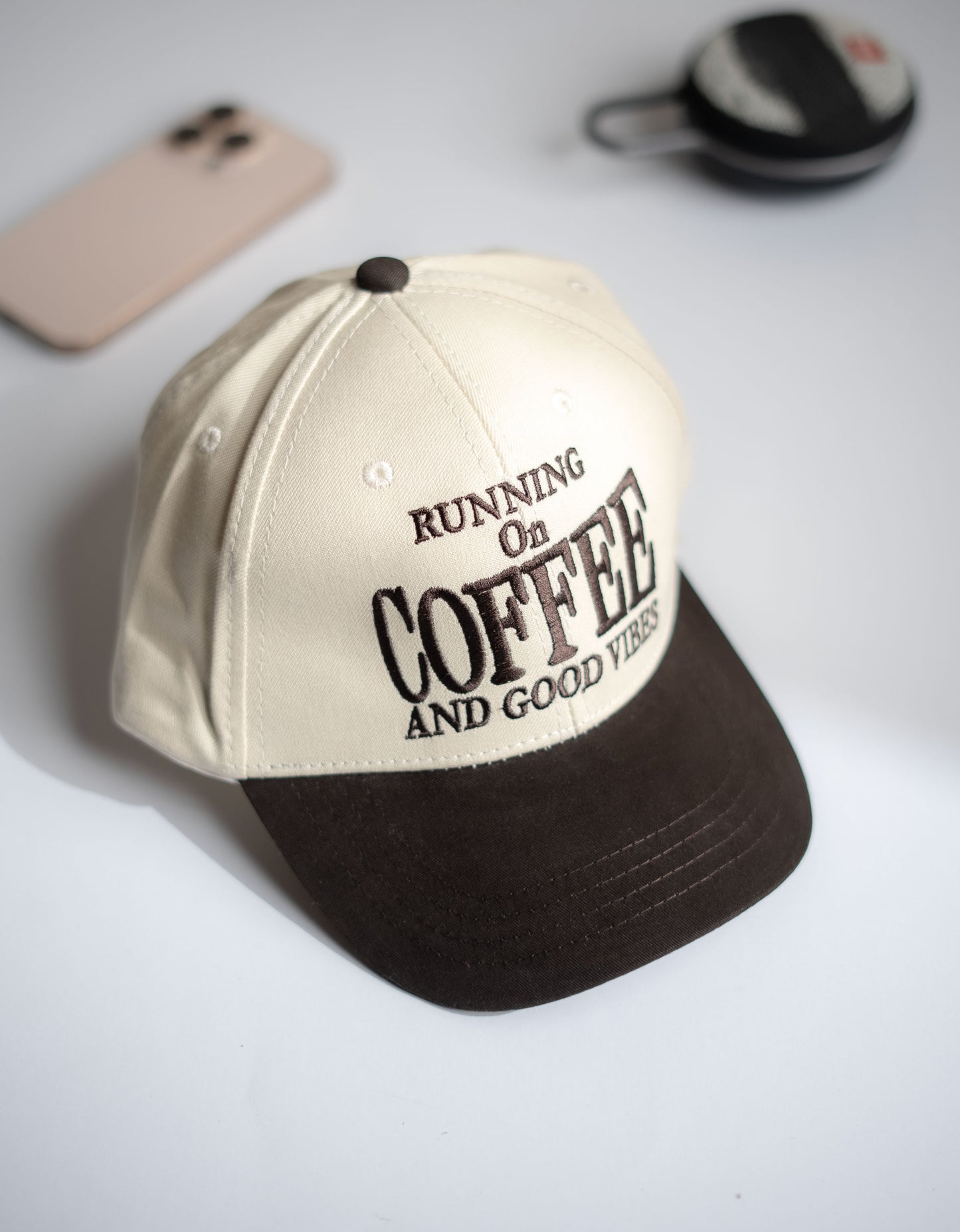 Beige and black cap with 'Running on Coffee and Good Vibes' text on a light gray background in Pakistan by Caps Nation