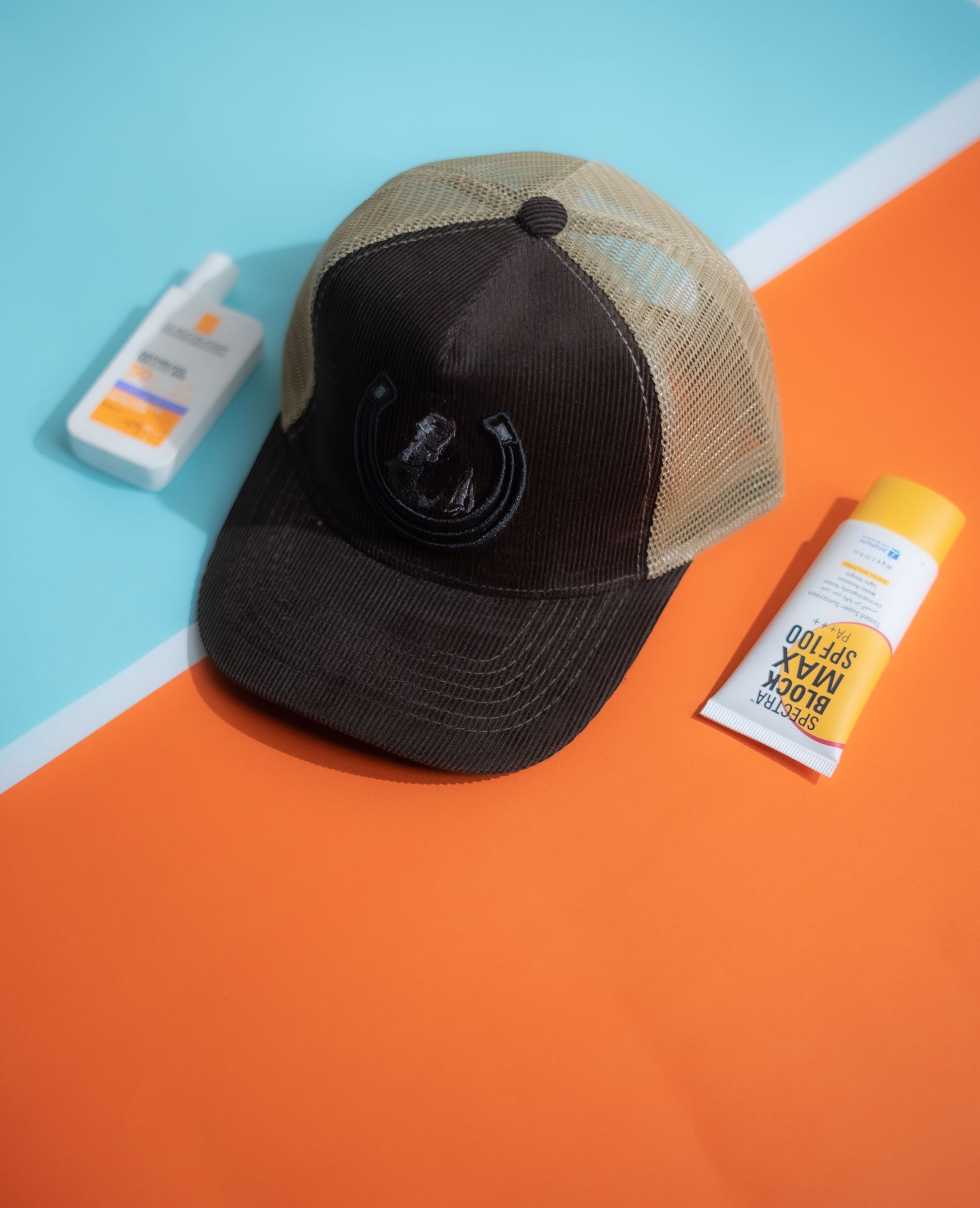 Black and beige cap on an orange and blue background with a bottle of sunscreen in Pakistan by Caps Nation