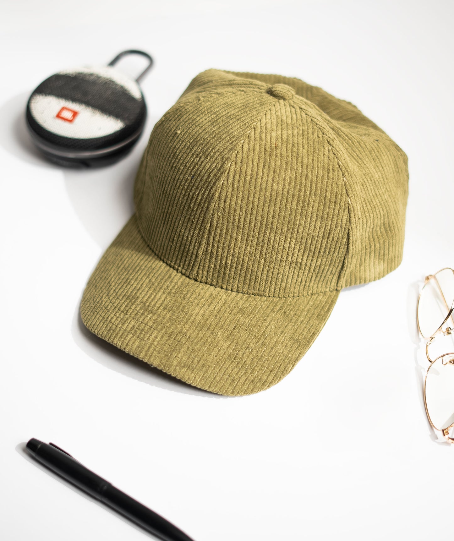 Green cap on a white surface with a pen, glasses, and a cup in the background in Pakistan by Caps Nation
