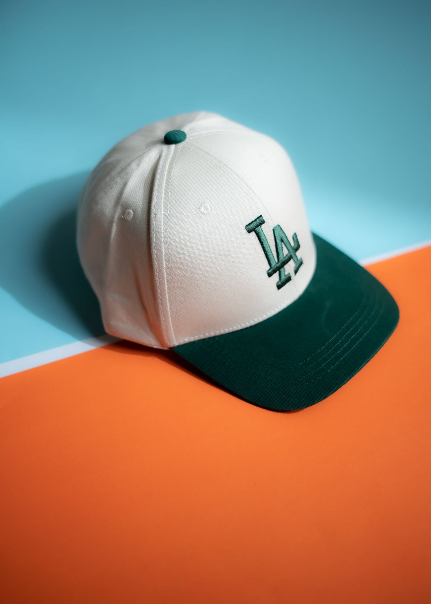 White baseball cap with green logo on a blue and orange background in Pakistan by Caps Nation