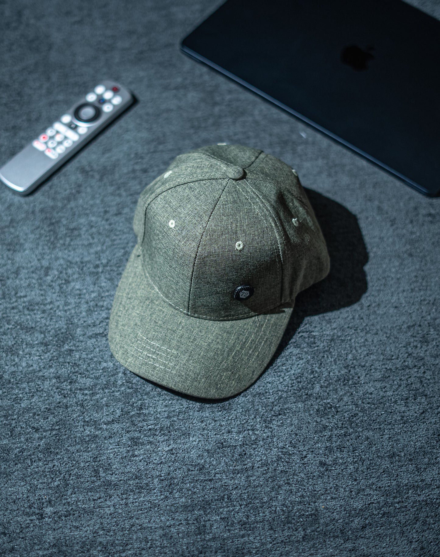 Green baseball cap on a dark textured surface with a remote control and electronic device in the background in Pakistan by Caps Nation