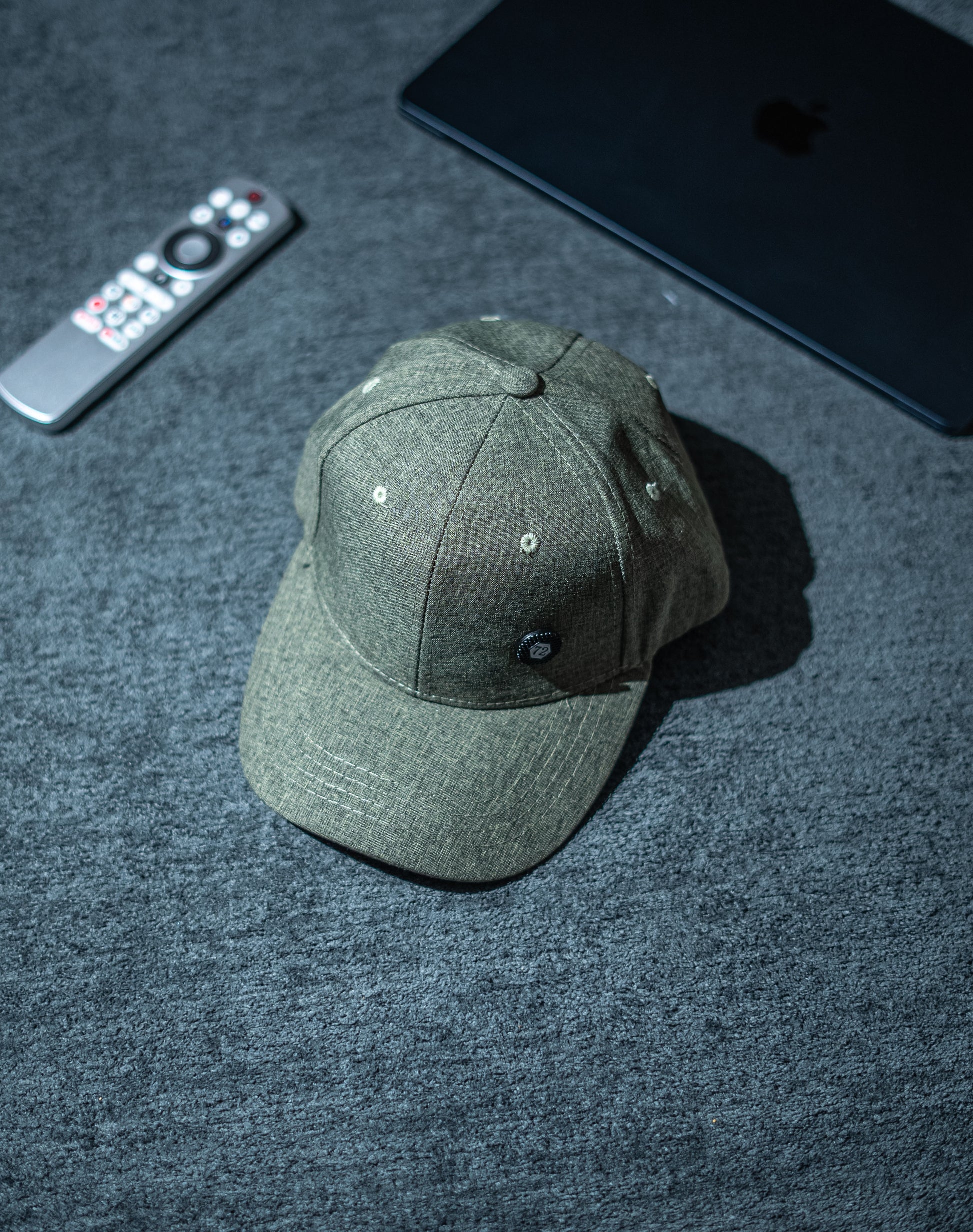 Green baseball cap on a dark textured surface with a remote control and electronic device in the background in Pakistan by Caps Nation