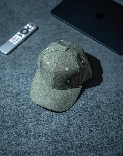 Green baseball cap on a dark textured surface with a remote control and electronic device in the background in Pakistan by Caps Nation