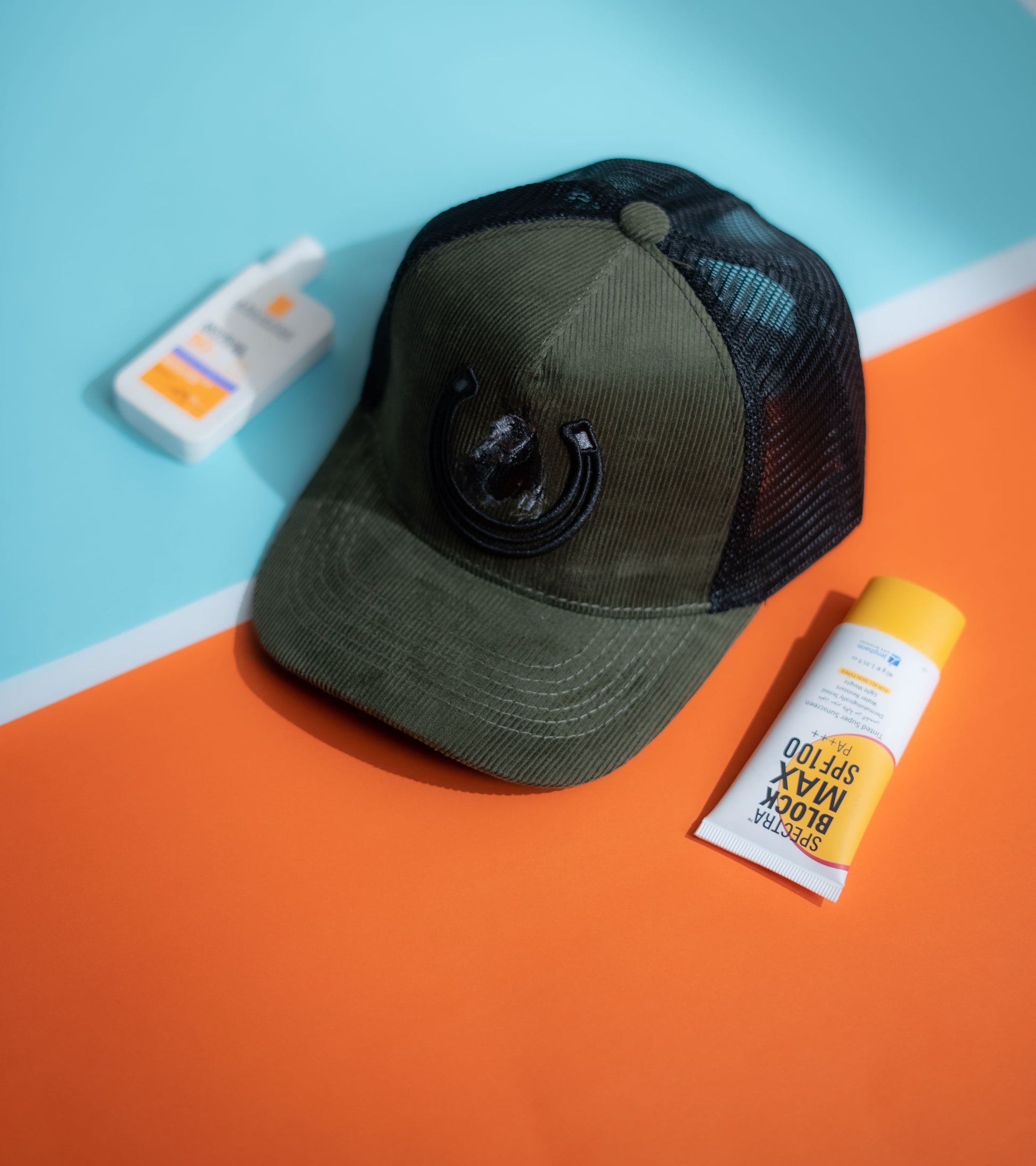 Green cap with black mesh back on an orange and blue background with sunscreen bottles in Pakistan by Caps Nation