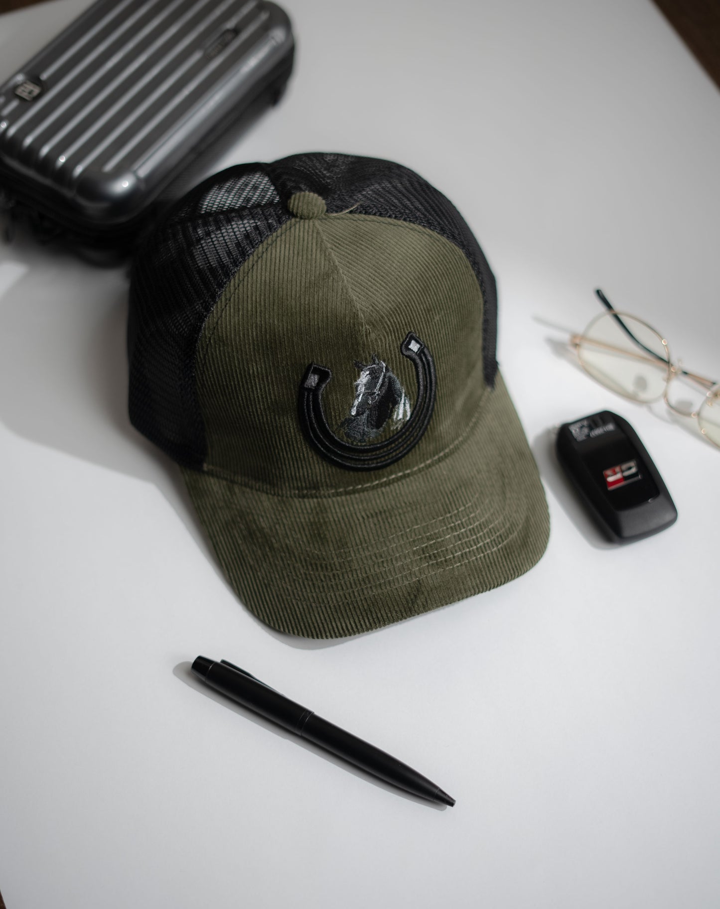 Green cap with black mesh back on a white surface with a pen, car key, and glasses in Pakistan by Caps Nation
