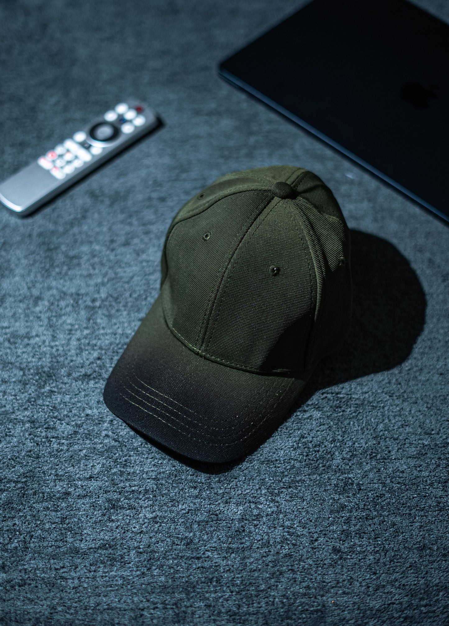 Green cap on a dark textured surface with a remote control and phone in the background in Pakistan by Caps Nation