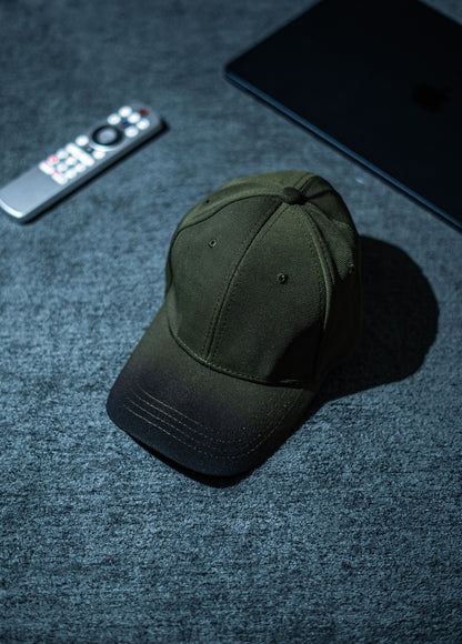 Green cap on a dark textured surface with a remote control and phone in the background in Pakistan by Caps Nation